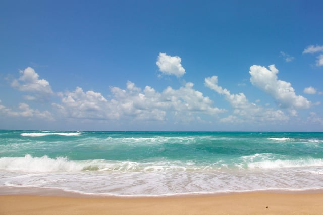 A Sandy Beach Next To Some Waves Under A Blue Sky
