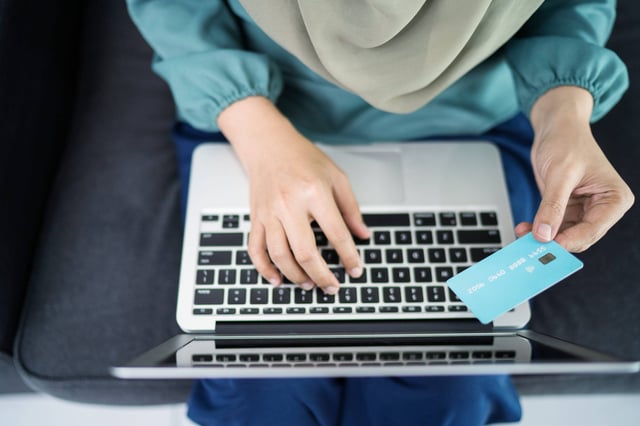 A Woman Using A Laptop Holding A Credit Card