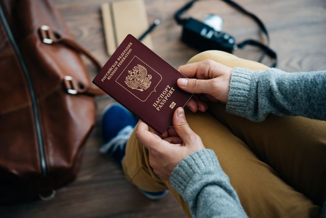 Person Holds Russian Travel Passport In Hand With Leather Bag And Photo