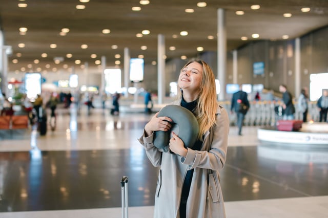 Woman Standing In Airport Hall With Valise And Neck Pillow