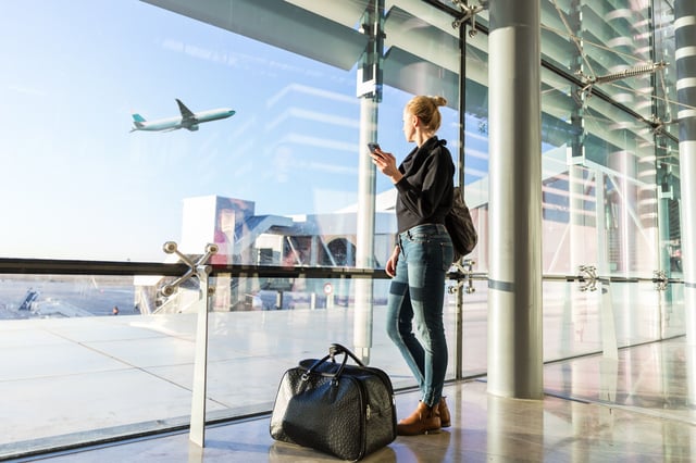 Young Casual Female Traveler At Airport Holding Smart Phone